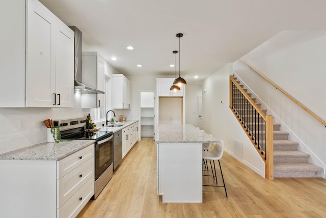 kitchen featuring stainless steel appliances, white cabinets, hanging light fixtures, a kitchen island, and light hardwood / wood-style flooring