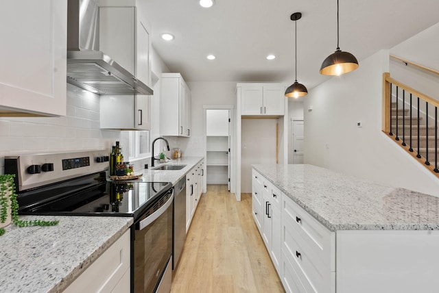 kitchen with stainless steel appliances, light hardwood / wood-style floors, wall chimney range hood, white cabinetry, and decorative light fixtures