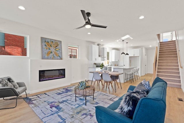 living room with light wood-type flooring, sink, and ceiling fan