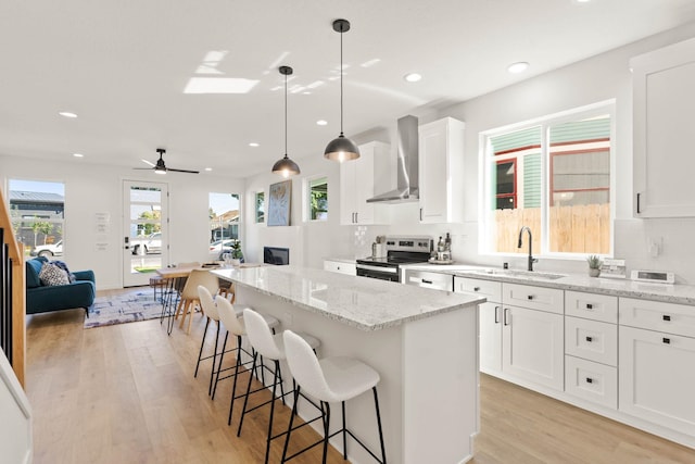 kitchen with stainless steel range with electric stovetop, a kitchen island, white cabinetry, sink, and wall chimney exhaust hood