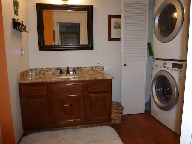 clothes washing area with stacked washer / dryer, sink, and wood-type flooring