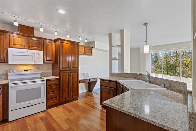 kitchen with light stone counters, light wood-type flooring, pendant lighting, sink, and white appliances