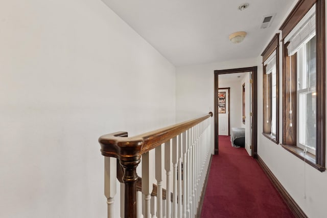 hallway with dark colored carpet and a healthy amount of sunlight