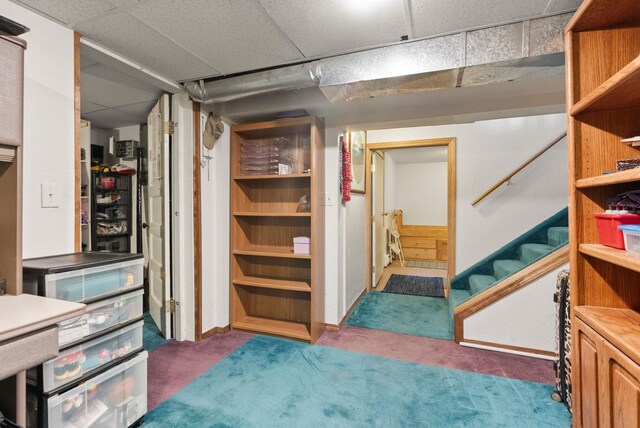 basement featuring a paneled ceiling and dark carpet