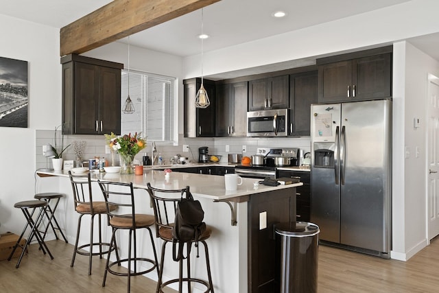 kitchen with stainless steel appliances, a kitchen breakfast bar, dark brown cabinets, light hardwood / wood-style flooring, and decorative light fixtures