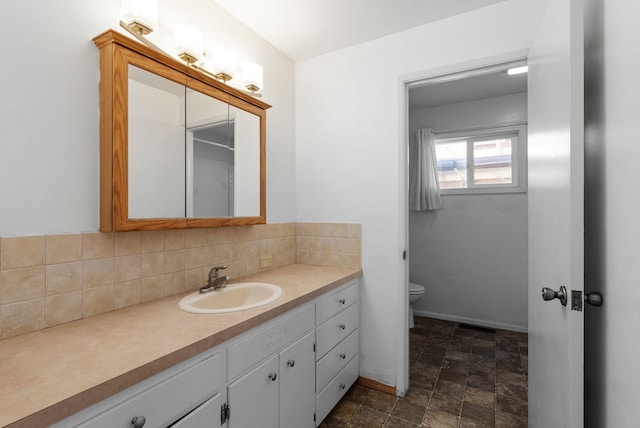 bathroom featuring baseboards, decorative backsplash, toilet, stone finish flooring, and vanity