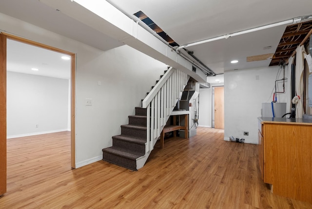 basement featuring light wood finished floors, stairway, and baseboards