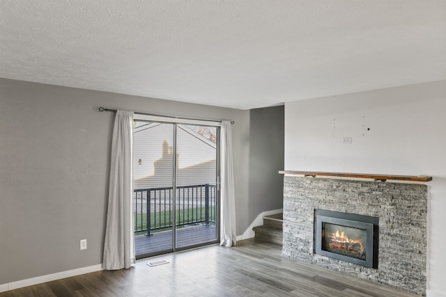 unfurnished living room with a stone fireplace, hardwood / wood-style floors, and a textured ceiling