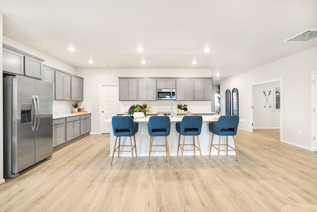 kitchen with a kitchen island with sink, light hardwood / wood-style floors, a breakfast bar, and appliances with stainless steel finishes