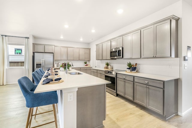 kitchen featuring stainless steel appliances, sink, a kitchen breakfast bar, an island with sink, and light wood-type flooring