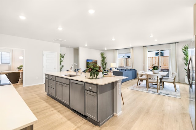 kitchen featuring a kitchen island with sink, sink, a breakfast bar area, dishwasher, and light hardwood / wood-style flooring