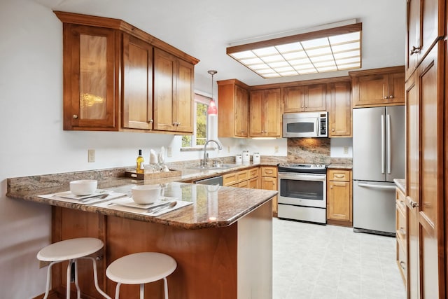 kitchen featuring kitchen peninsula, sink, a breakfast bar area, pendant lighting, and appliances with stainless steel finishes