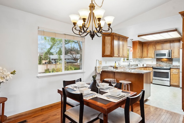 dining space with light wood-type flooring, sink, an inviting chandelier, and lofted ceiling