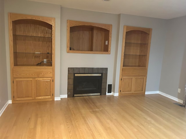 unfurnished living room featuring built in shelves, light wood-type flooring, and a tiled fireplace