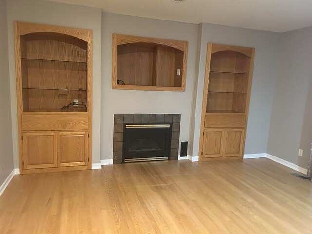 unfurnished living room featuring built in shelves, light hardwood / wood-style floors, and a tile fireplace