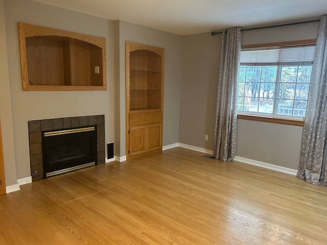 unfurnished living room with light wood-type flooring and a tile fireplace