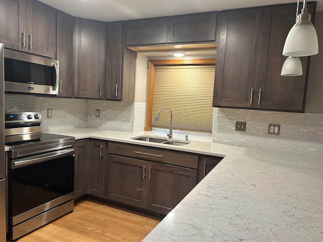 kitchen featuring light hardwood / wood-style floors, stainless steel appliances, hanging light fixtures, sink, and backsplash