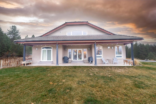 back house at dusk featuring a lawn and a patio