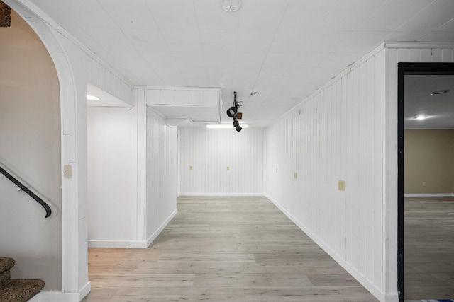 hallway featuring ornamental molding, light wood-type flooring, and wooden walls