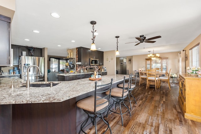 kitchen featuring dark brown cabinetry, light stone countertops, dark hardwood / wood-style floors, decorative light fixtures, and appliances with stainless steel finishes