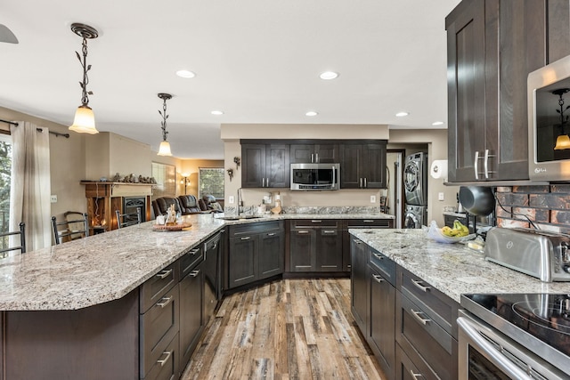 kitchen featuring pendant lighting, stacked washer and dryer, light hardwood / wood-style floors, a kitchen bar, and stainless steel appliances