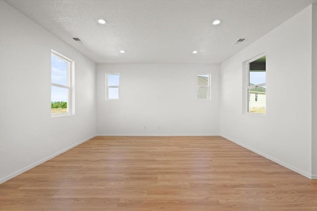 empty room with a textured ceiling and light hardwood / wood-style flooring