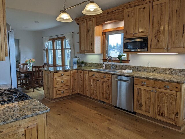 kitchen featuring kitchen peninsula, appliances with stainless steel finishes, light wood-type flooring, sink, and pendant lighting