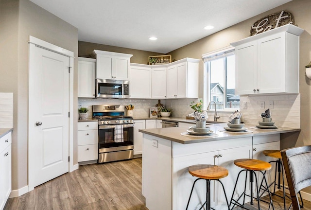 kitchen with stainless steel appliances, white cabinetry, tasteful backsplash, and light hardwood / wood-style floors