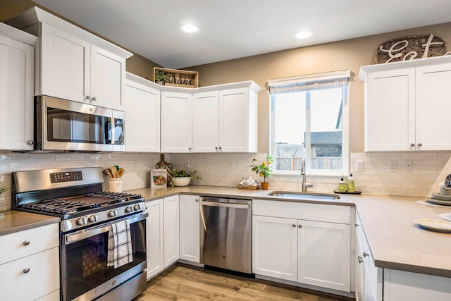 kitchen with white cabinets, sink, decorative backsplash, light wood-type flooring, and appliances with stainless steel finishes