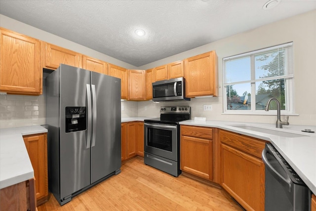 kitchen with sink, stainless steel appliances, a textured ceiling, decorative backsplash, and light wood-type flooring