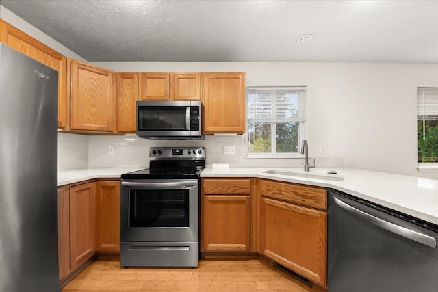 kitchen featuring sink, stainless steel appliances, backsplash, light hardwood / wood-style floors, and a textured ceiling