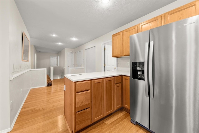 kitchen with light brown cabinets, stainless steel refrigerator with ice dispenser, kitchen peninsula, light hardwood / wood-style floors, and a textured ceiling