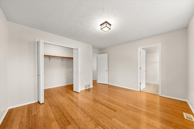 unfurnished bedroom featuring hardwood / wood-style floors, a textured ceiling, ensuite bathroom, and a closet