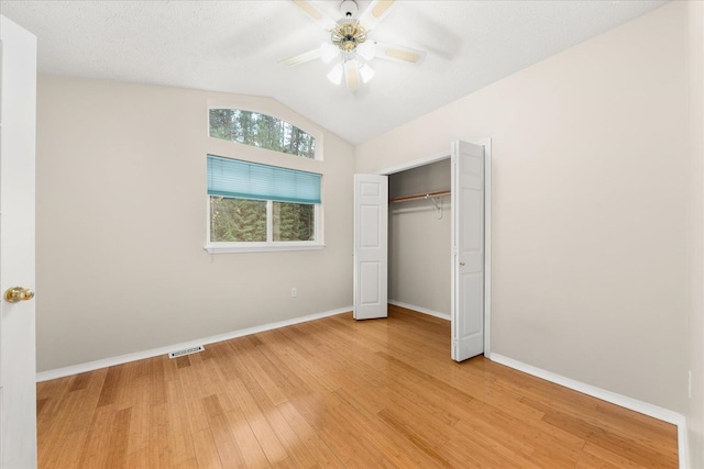 unfurnished bedroom with lofted ceiling, hardwood / wood-style flooring, ceiling fan, a textured ceiling, and a closet