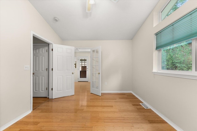 unfurnished room featuring lofted ceiling, light wood-type flooring, french doors, and a healthy amount of sunlight