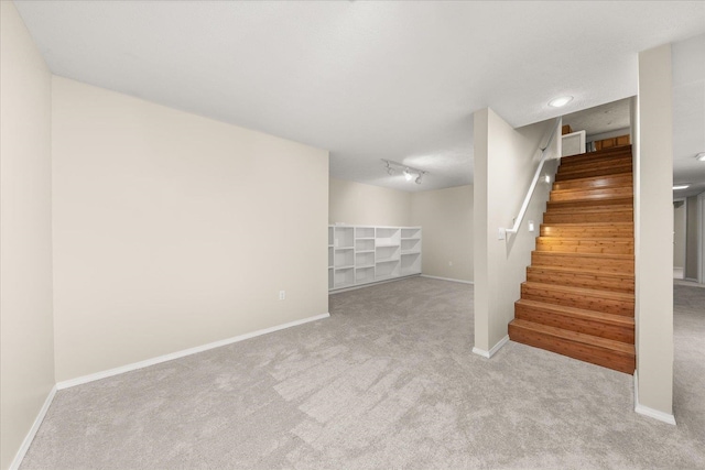 basement with rail lighting and light colored carpet