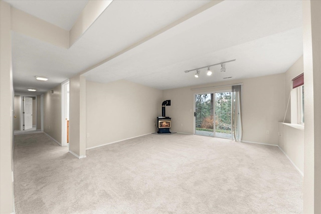 spare room with a wood stove, light carpet, and track lighting