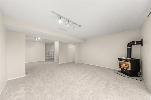 basement with rail lighting, light colored carpet, and a wood stove