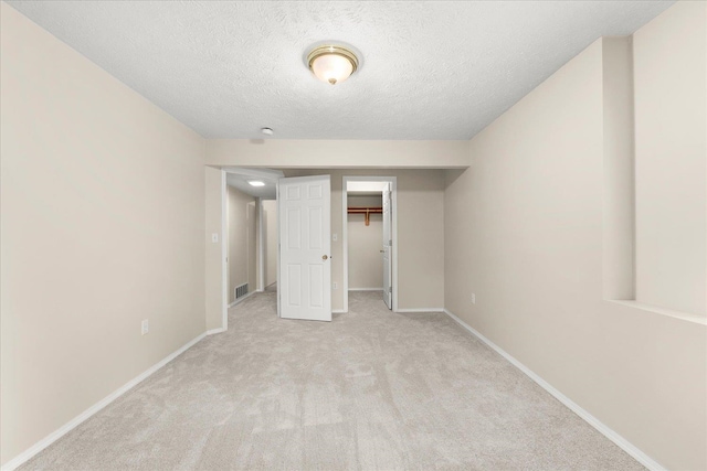 unfurnished bedroom featuring light carpet, a textured ceiling, a spacious closet, and a closet