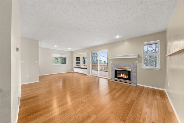 unfurnished living room featuring a tiled fireplace, plenty of natural light, and light wood-type flooring