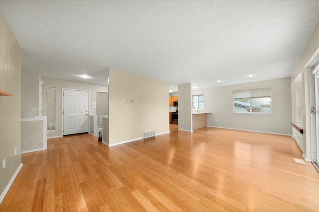 unfurnished living room featuring a textured ceiling, light hardwood / wood-style flooring, and sink