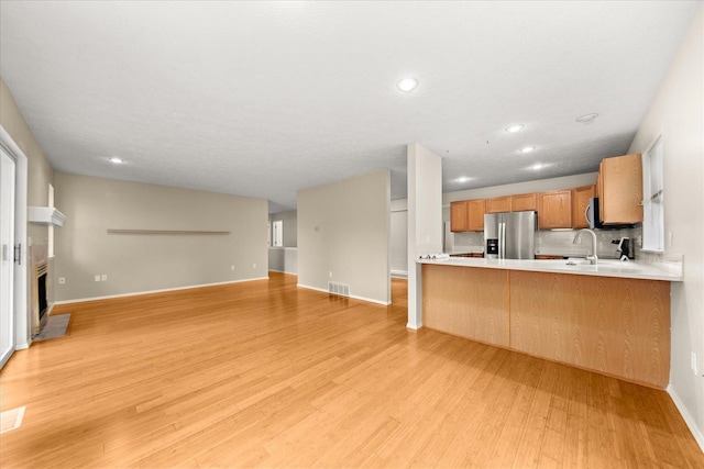 kitchen featuring sink, stainless steel fridge with ice dispenser, kitchen peninsula, light hardwood / wood-style floors, and decorative backsplash