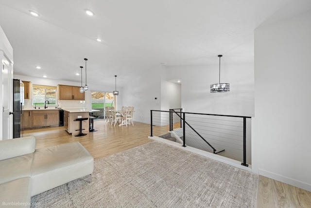 living room with sink, light hardwood / wood-style flooring, vaulted ceiling, and a notable chandelier