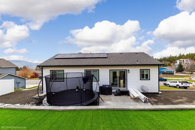 rear view of house with a yard, solar panels, a trampoline, a mountain view, and a patio