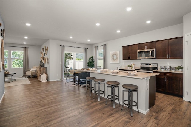 kitchen featuring a breakfast bar, dark wood-type flooring, an island with sink, appliances with stainless steel finishes, and dark brown cabinets