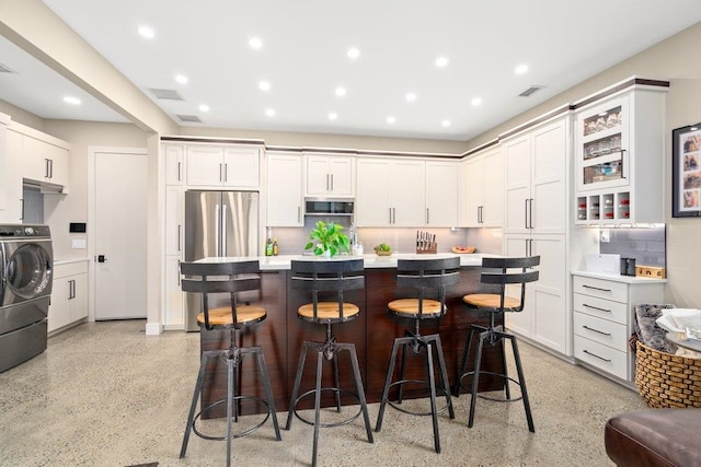 kitchen with a kitchen breakfast bar, stainless steel appliances, white cabinets, washer / dryer, and a center island