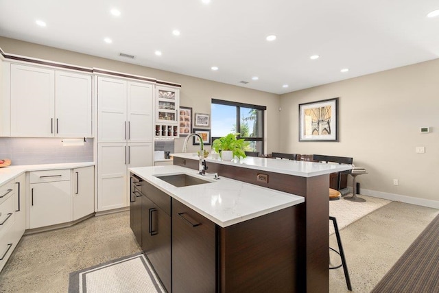 kitchen featuring a breakfast bar, backsplash, white cabinets, sink, and an island with sink