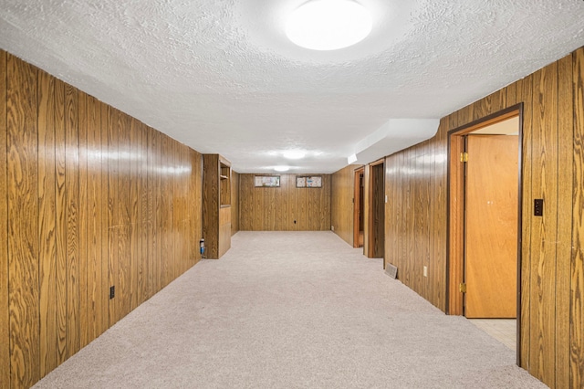 hallway with light carpet, wooden walls, and a textured ceiling