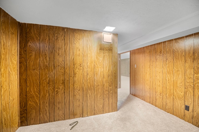 unfurnished room with a textured ceiling, wood walls, and light carpet