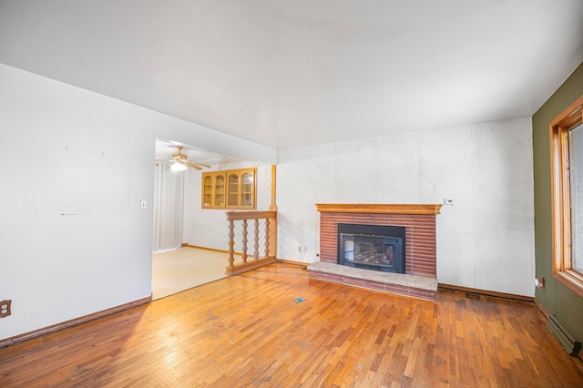 unfurnished living room featuring ceiling fan, a fireplace, a baseboard heating unit, and hardwood / wood-style flooring